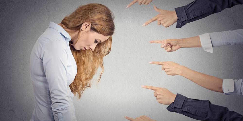 Frau senkt den Kopf, während mehrere Hände auf sie zeigen – Symbol für Schuldzuweisung
